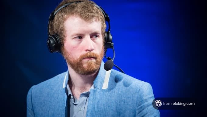 A focused esports commentator wearing a blue jacket and headset.