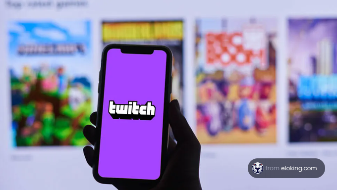 Person holding a smartphone displaying Twitch logo with blurred game posters in the background