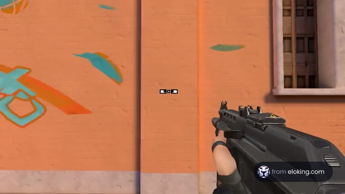 A person holding a gun in front of an orange wall with graffiti.