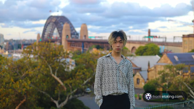 Un joven con una camisa de estampado de pie frente al Puente de Sydney.