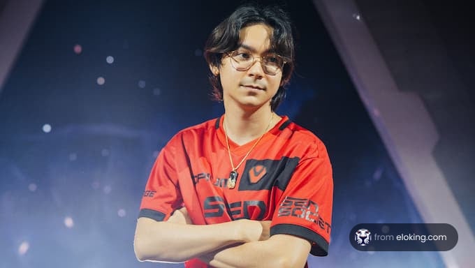 A young esports player poses confidently in a red shirt.