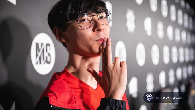 Young man in a red jacket making a thinking gesture at a black logo wall event